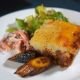 An elevated interpretation of the classic comfort dish, featuring perfectly browned potato crust, served with caramelized plantains and fresh garden salad. The plating transforms homestyle cooking into fine dining.