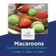 Elegant macarons in bold red and green hues, displayed in luxurious gold packaging. The lighting captures the delicate texture of these French delicacies while highlighting their perfect form and festive colors.