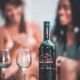Lifestyle shot of Pierre Marcel wine in a social setting, with softly blurred figures creating an intimate atmosphere. The moody lighting and bokeh effect capture the warmth of shared moments.